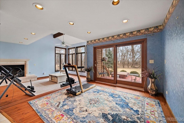 exercise room featuring a fireplace with raised hearth, wood finished floors, recessed lighting, baseboards, and vaulted ceiling