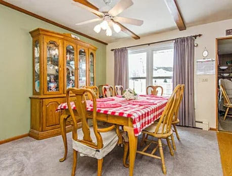 dining space with beamed ceiling, a ceiling fan, crown molding, baseboards, and light colored carpet