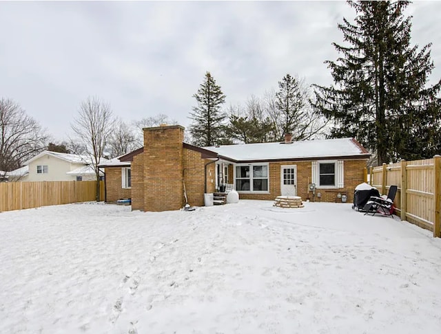 snow covered rear of property featuring brick siding, a chimney, and a fenced backyard