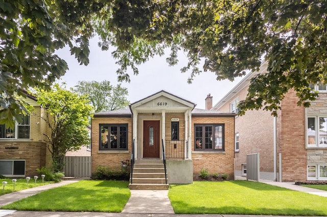 view of front facade with brick siding, a chimney, a front yard, and fence