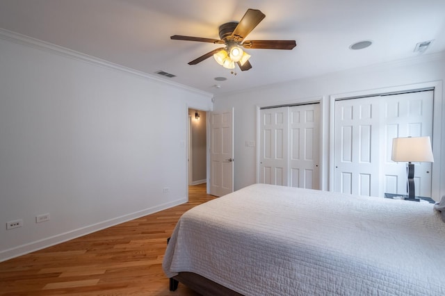 bedroom featuring crown molding, multiple closets, visible vents, light wood-style floors, and baseboards