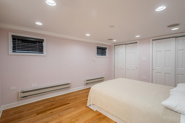 bedroom with a baseboard radiator, light wood-style flooring, baseboard heating, multiple closets, and recessed lighting