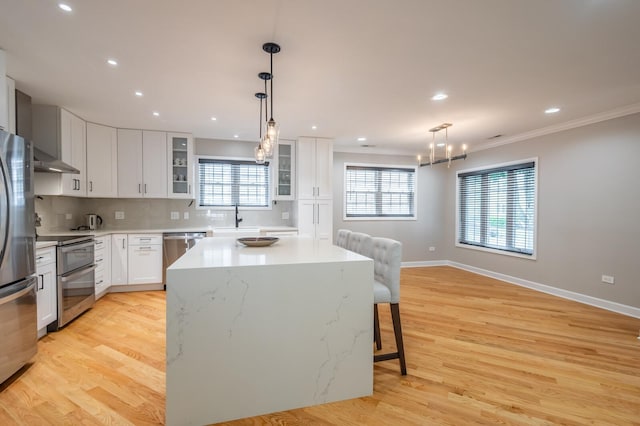 kitchen with stainless steel appliances, a kitchen island, light wood-style floors, ornamental molding, and decorative backsplash