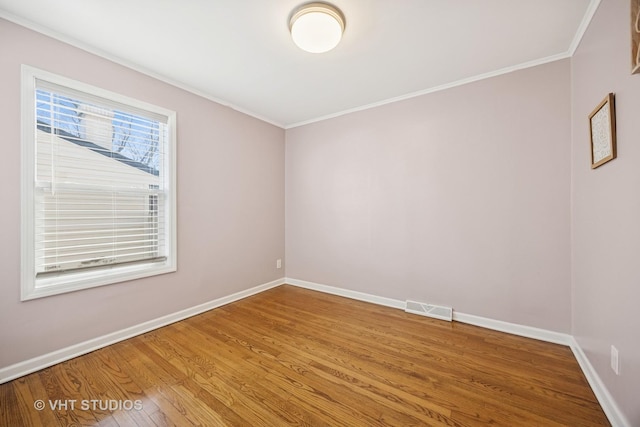 empty room with crown molding, wood finished floors, visible vents, and baseboards