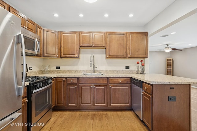 kitchen featuring light wood finished floors, appliances with stainless steel finishes, a peninsula, a ceiling fan, and a sink