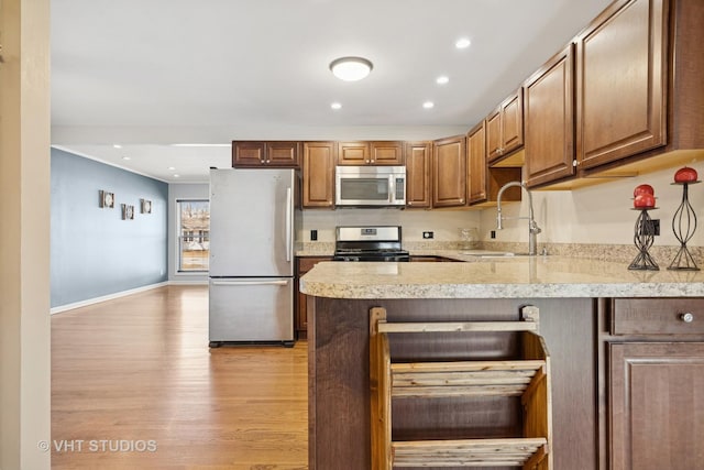 kitchen featuring light countertops, a peninsula, light wood-style floors, stainless steel appliances, and a sink