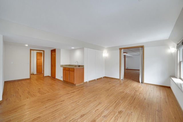 unfurnished living room featuring indoor wet bar, light wood-style floors, and baseboards