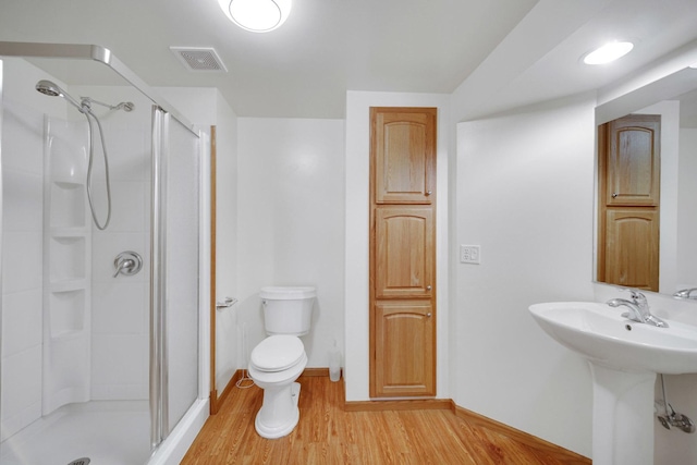 bathroom with a shower stall, toilet, wood finished floors, and visible vents