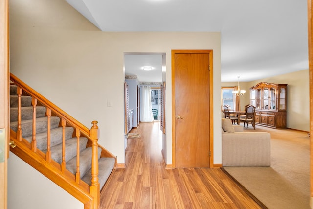 hallway featuring light wood finished floors, a notable chandelier, stairs, and baseboards