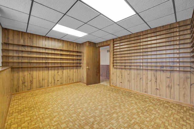 unfurnished room featuring a drop ceiling, baseboards, and wood walls