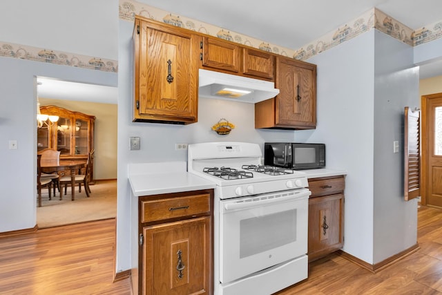 kitchen featuring light wood finished floors, white gas stove, light countertops, under cabinet range hood, and black microwave