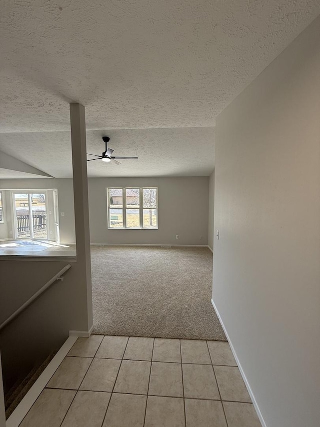 spare room with light carpet, light tile patterned floors, baseboards, a ceiling fan, and a textured ceiling