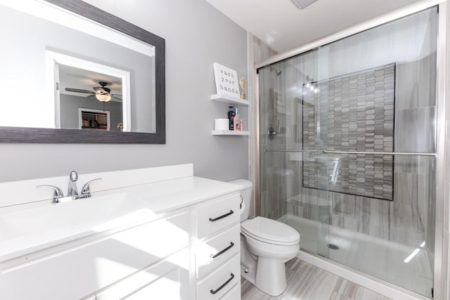 bathroom with a ceiling fan, vanity, a shower stall, and toilet