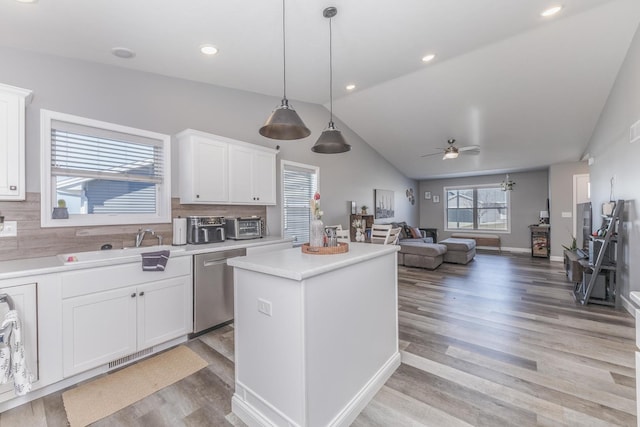 kitchen featuring a kitchen island, light countertops, lofted ceiling, stainless steel dishwasher, and a sink