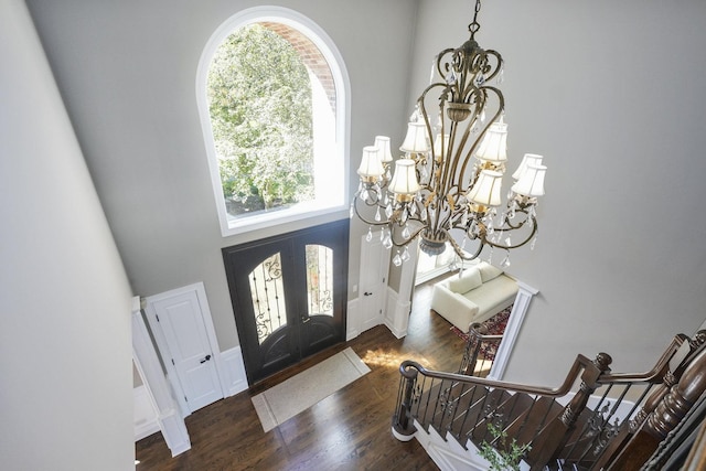 entrance foyer with stairs, french doors, a high ceiling, wood finished floors, and a notable chandelier