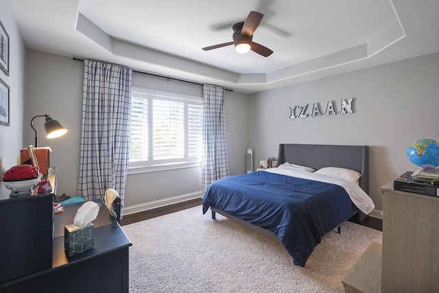 bedroom with a raised ceiling, wood finished floors, a ceiling fan, and baseboards