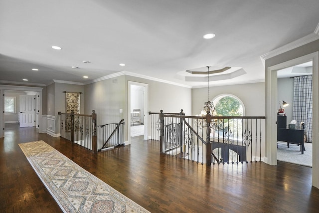 hallway with a tray ceiling, wood finished floors, an upstairs landing, and ornamental molding