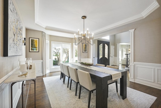 dining area with dark wood-type flooring, ornamental molding, wainscoting, and a decorative wall