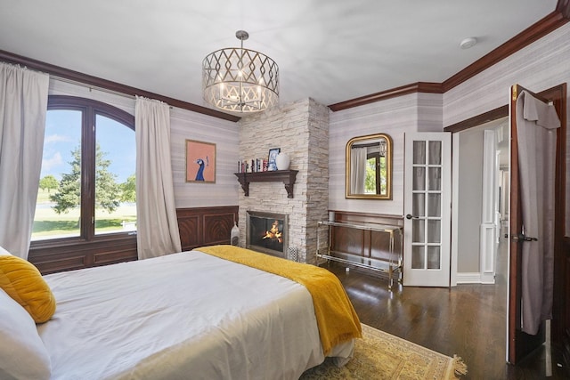 bedroom featuring an inviting chandelier, a stone fireplace, wood finished floors, and ornamental molding