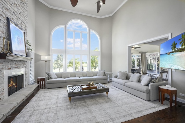 living area with a ceiling fan, wood finished floors, a fireplace, ornamental molding, and a towering ceiling