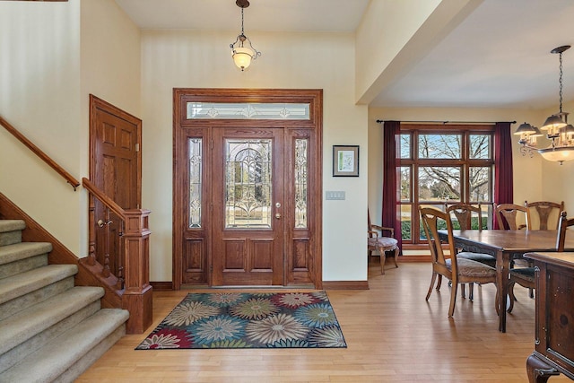 foyer with baseboards, a notable chandelier, light wood-style flooring, and stairs