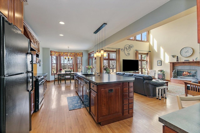 kitchen with black appliances, a sink, dark countertops, a glass covered fireplace, and light wood finished floors