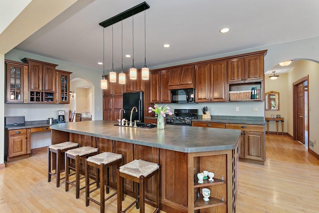 kitchen featuring black appliances, light wood-style flooring, open shelves, dark countertops, and arched walkways