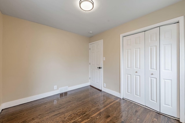 unfurnished bedroom with visible vents, a closet, baseboards, and dark wood-style flooring