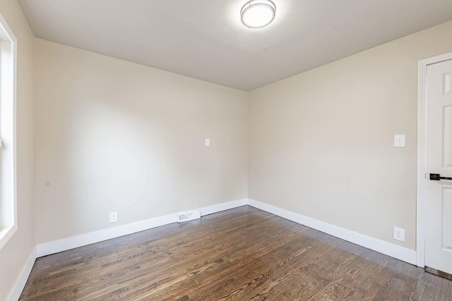 empty room with baseboards, visible vents, and dark wood finished floors