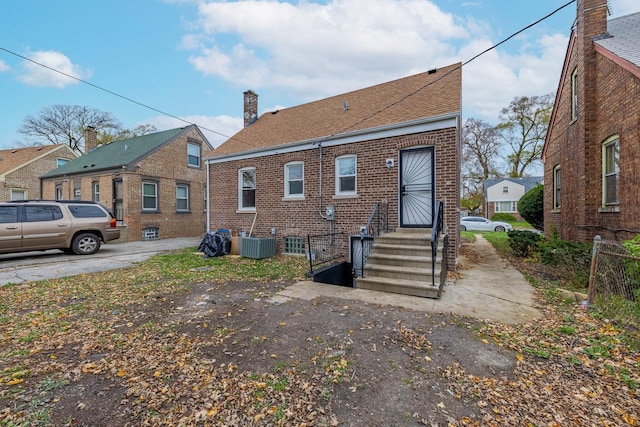 rear view of property with brick siding, roof with shingles, and central air condition unit