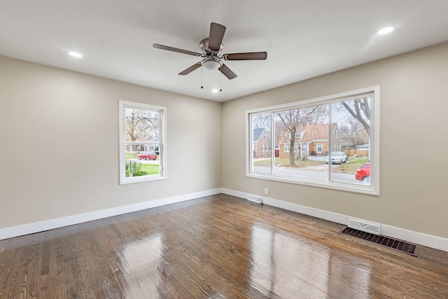 empty room with wood finished floors, visible vents, and baseboards