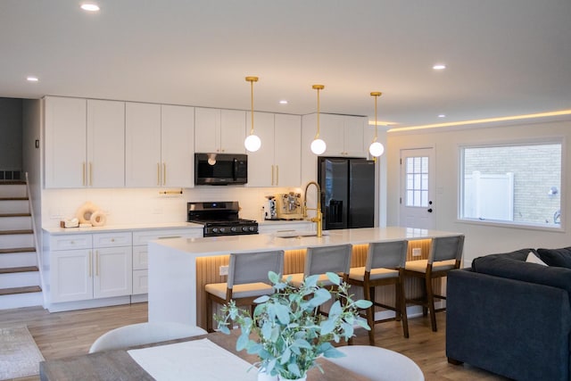 kitchen featuring light wood finished floors, black refrigerator with ice dispenser, gas stove, open floor plan, and a sink