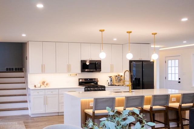 kitchen with appliances with stainless steel finishes, a kitchen island with sink, light countertops, white cabinetry, and a sink