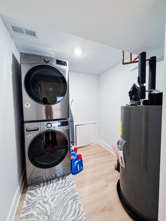 clothes washing area featuring laundry area, visible vents, light wood-style floors, water heater, and stacked washer / drying machine