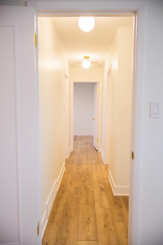 hall with visible vents, light wood-style flooring, and baseboards