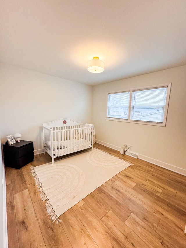 unfurnished bedroom featuring a nursery area, baseboards, and wood finished floors