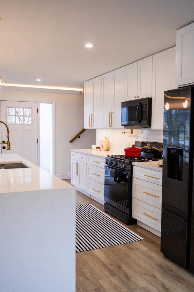 kitchen with light wood finished floors, decorative backsplash, black appliances, white cabinetry, and a sink