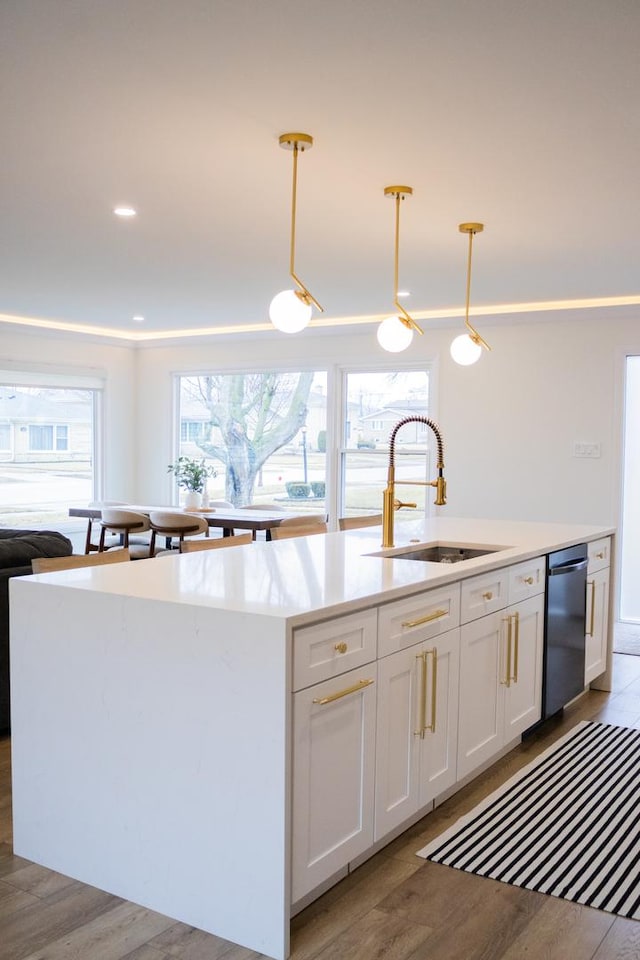 kitchen with light countertops, white cabinetry, a sink, a kitchen island with sink, and dishwasher