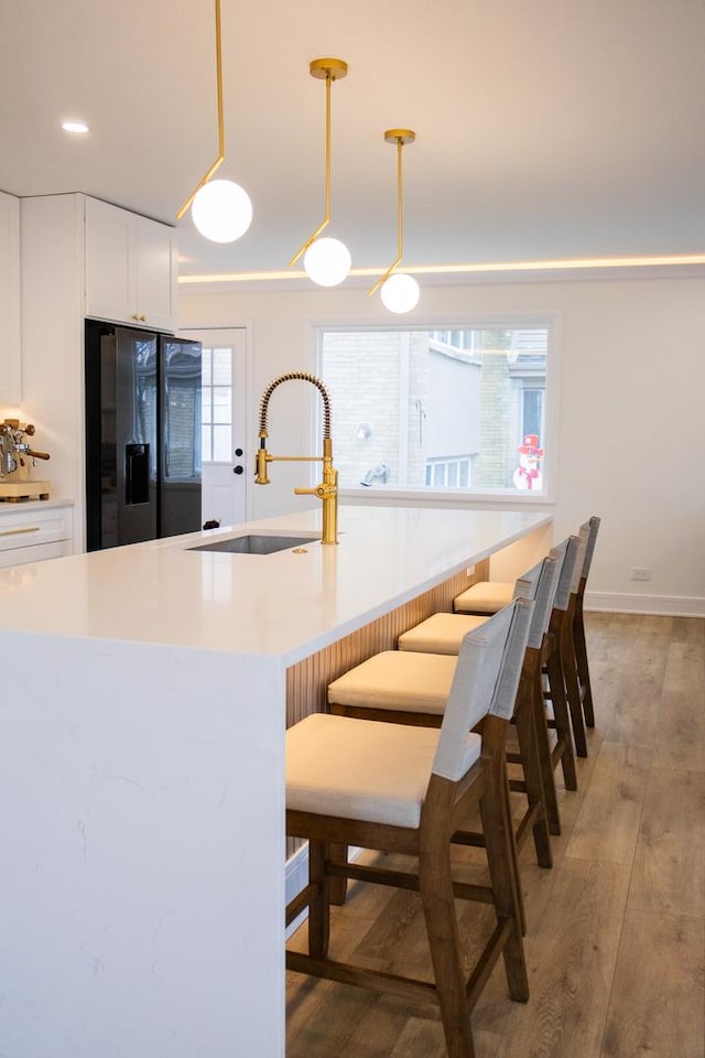 kitchen featuring light wood-style flooring, a sink, black fridge with ice dispenser, white cabinetry, and light countertops