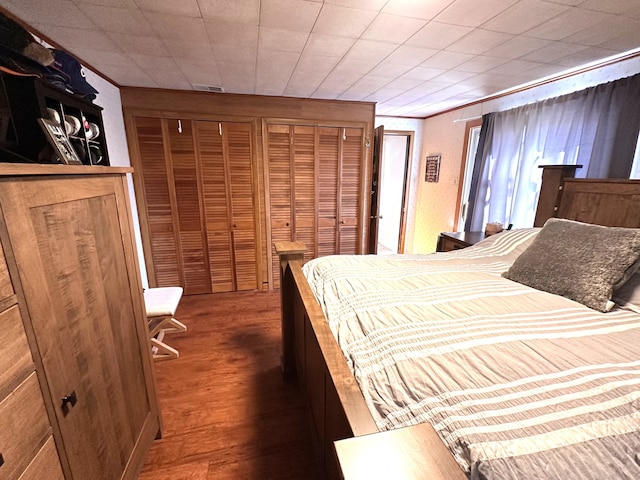 bedroom featuring ornamental molding, wood finished floors, visible vents, and multiple closets