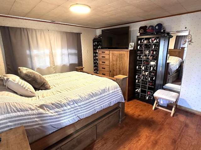 bedroom with ornamental molding, wallpapered walls, and wood finished floors