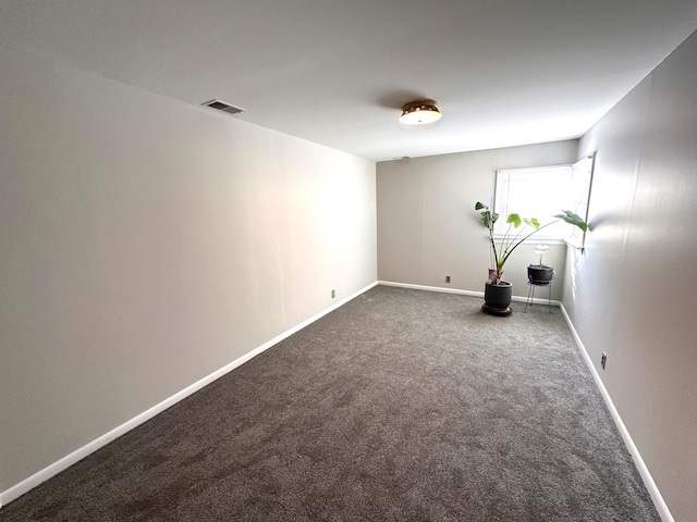 empty room with dark colored carpet, visible vents, and baseboards