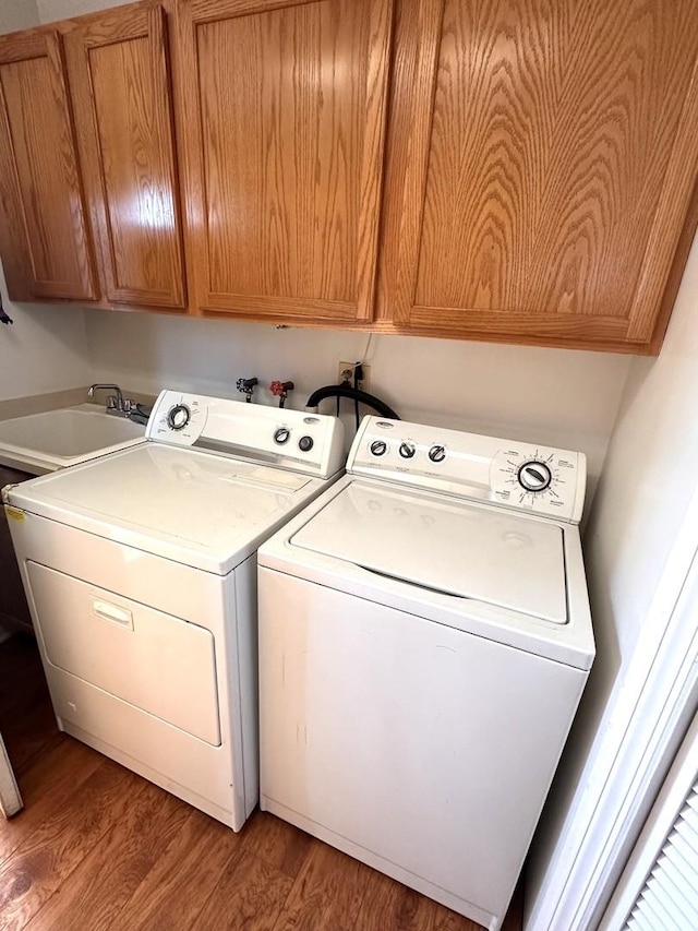 clothes washing area featuring cabinet space, light wood-style flooring, washer and clothes dryer, and a sink