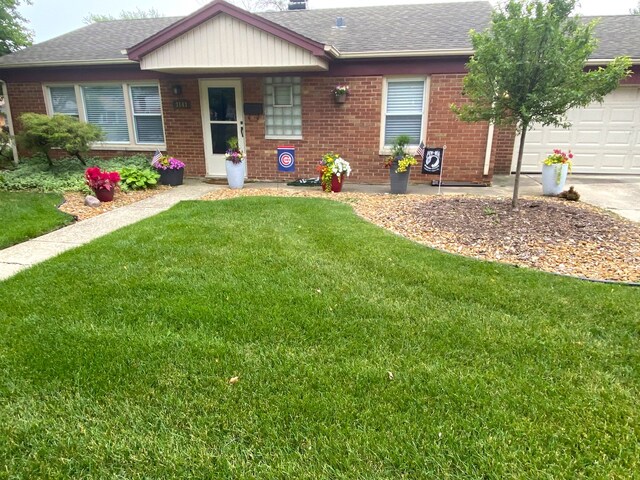 single story home featuring a garage, brick siding, a front lawn, and roof with shingles