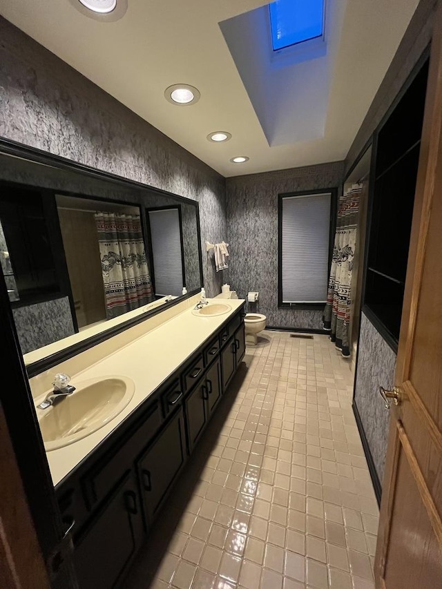 bathroom featuring wallpapered walls, double vanity, toilet, and a sink