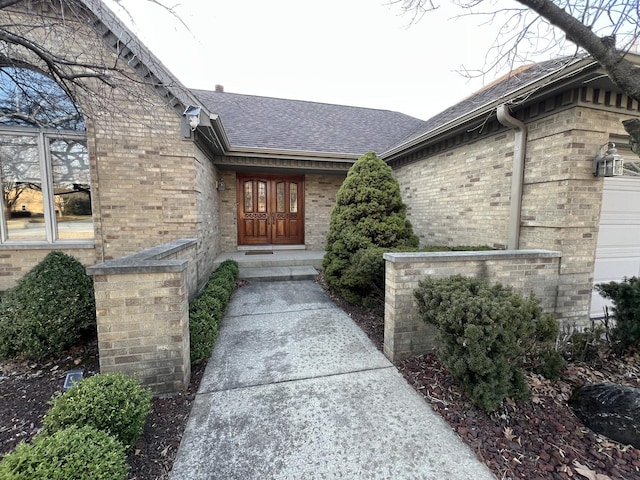 doorway to property with brick siding and a shingled roof