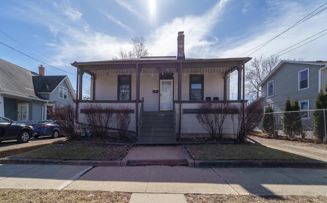 bungalow-style house with covered porch, a chimney, and fence