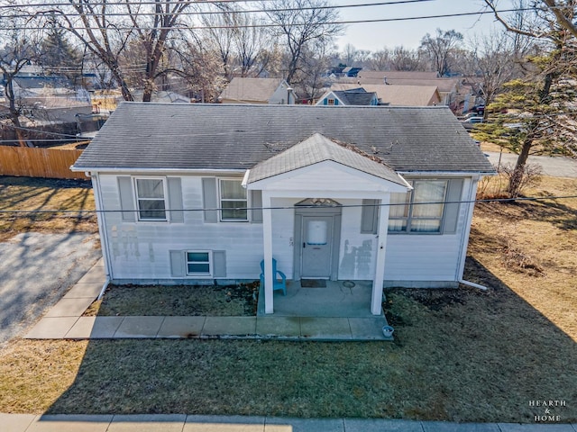 view of front of house with a front lawn, roof with shingles, and fence