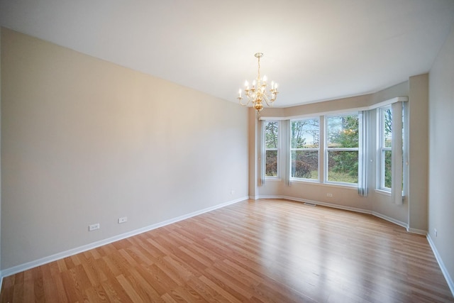 spare room with light wood-type flooring, baseboards, and a chandelier