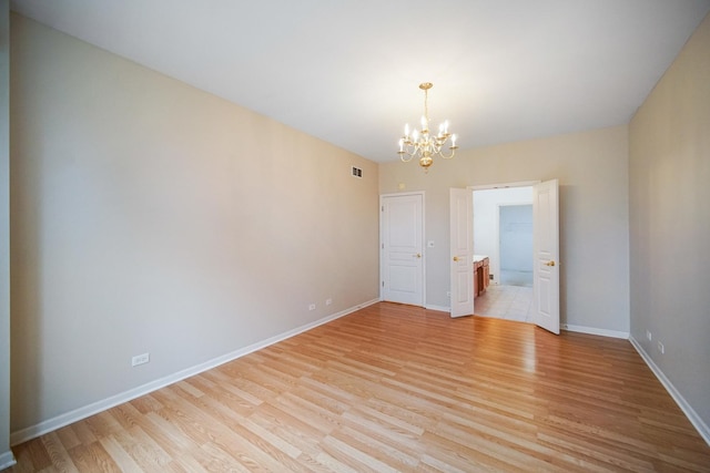 empty room with an inviting chandelier, light wood-style flooring, visible vents, and baseboards